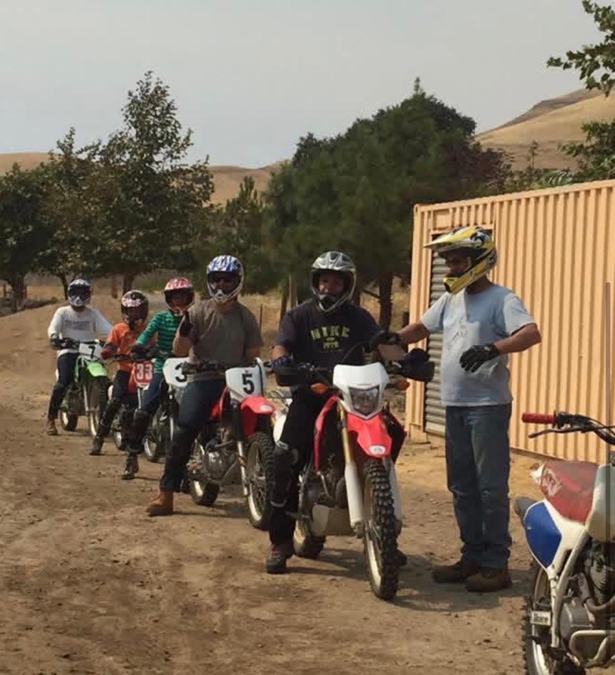 An instructor in a yellow helmet guiding a line of students seated on their dirt bikes